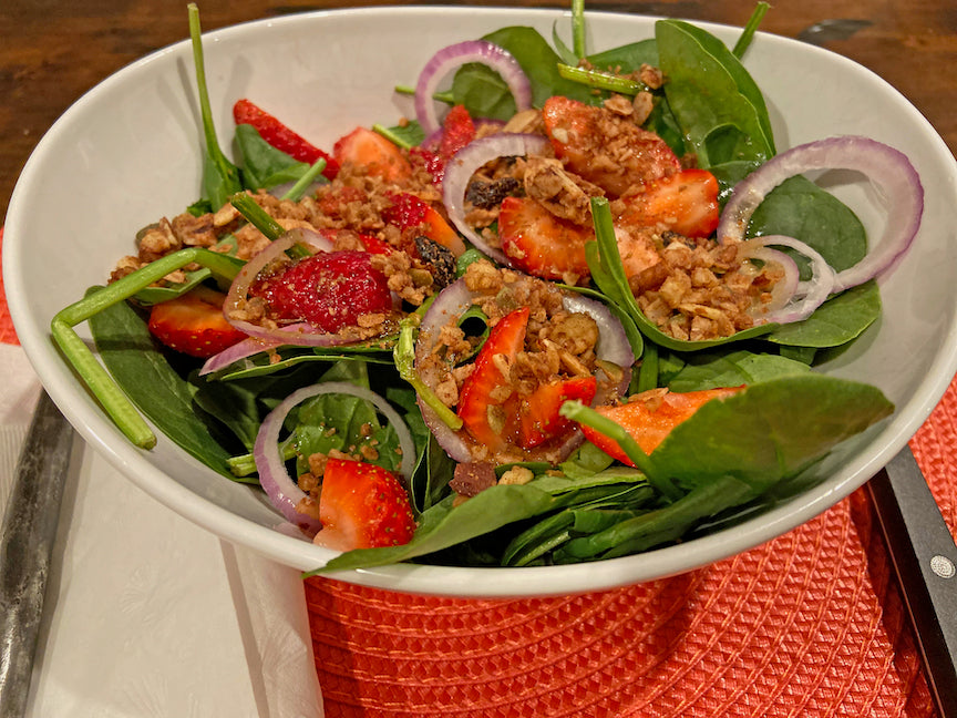 Photo of a spinach salad with a vinaigrette dressing, red onions, strawberries, and Cherry Berry JuNūla Just Nuts Granola