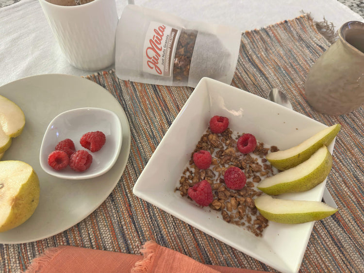 Breakfast scene with a bowl of cappuccino Italiano granola, fruit, and raspberries on a table.